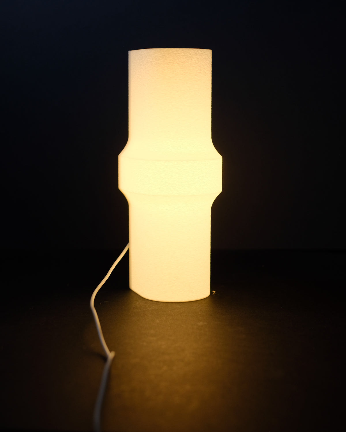 Minimalist Bulge LED Lamp tall cylinder form distinctive waist-pinch middle bulge profile glowing warm amber light translucent white finish pure black studio background slight angle atmospheric product hero shot