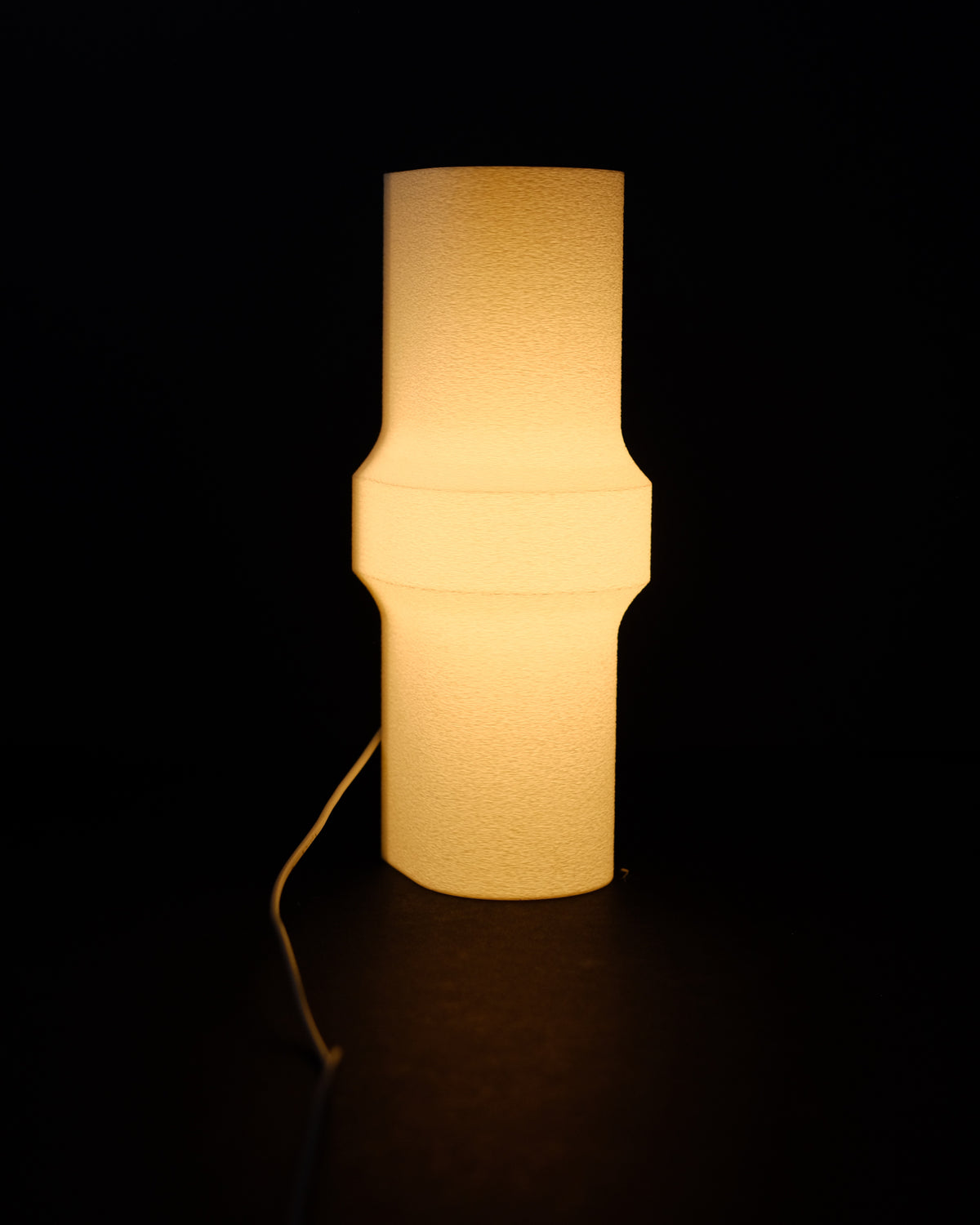 Minimalist Bulge LED Lamp tall cylinder form distinctive waist-pinch middle bulge profile glowing warm amber light translucent white finish pure black studio background atmospheric product hero shot
