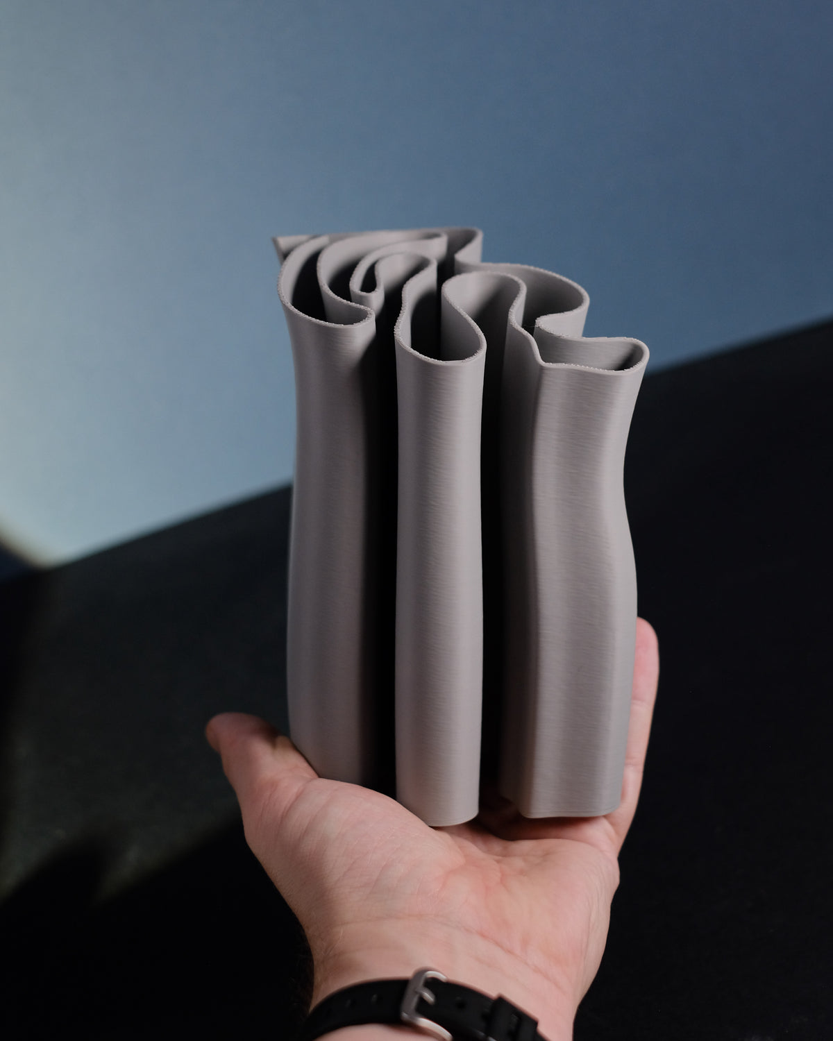 Fabric Ripple Vase and Desktop Organizer tall cluster undulating fabric-fold tube forms sinuous wavy ripple rim warm grey taupe matte finish held in hand showing scale and organic ripple detail editorial scale shot