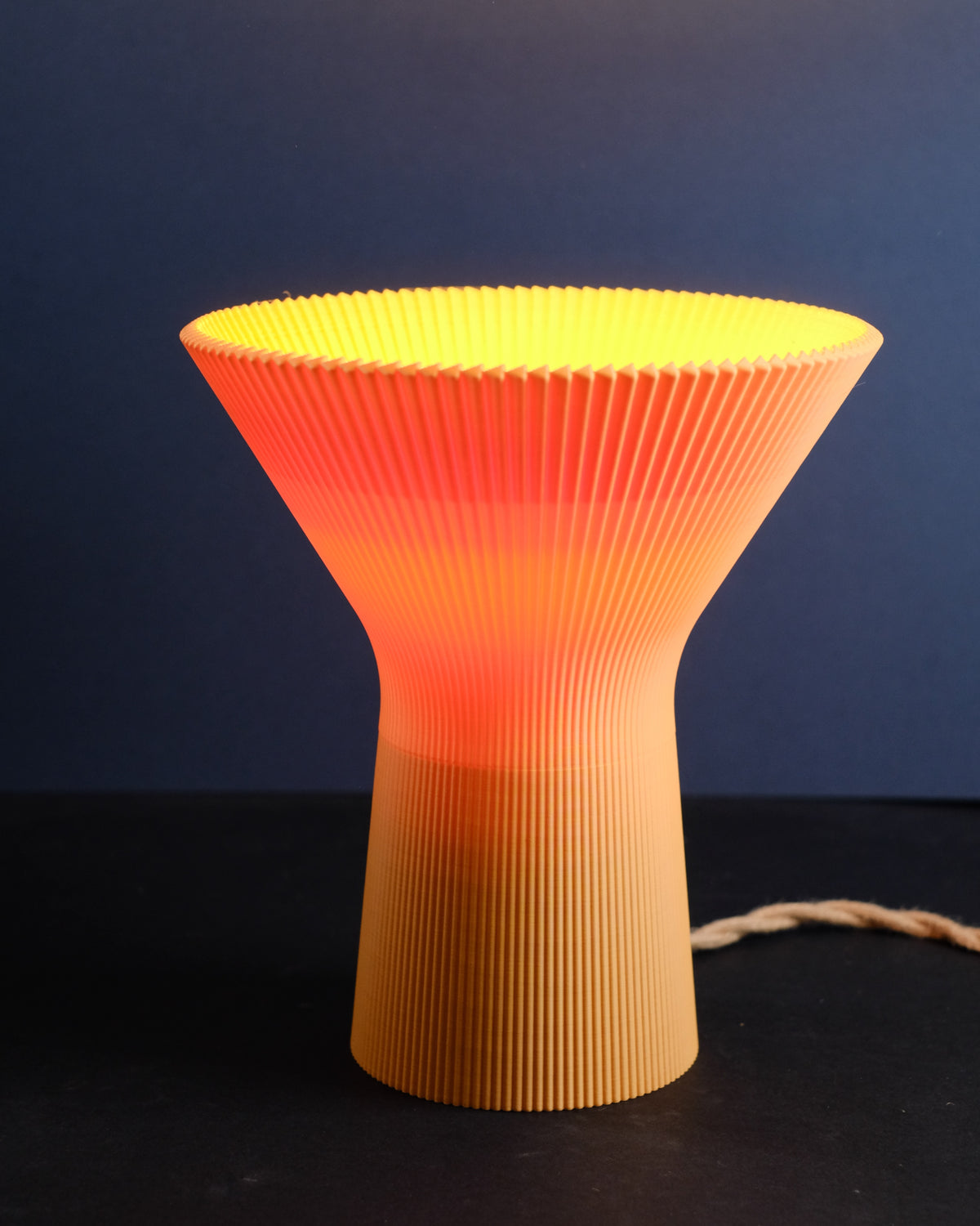 Hand holding the orange pleated inverted funnel lamp against a dark background.