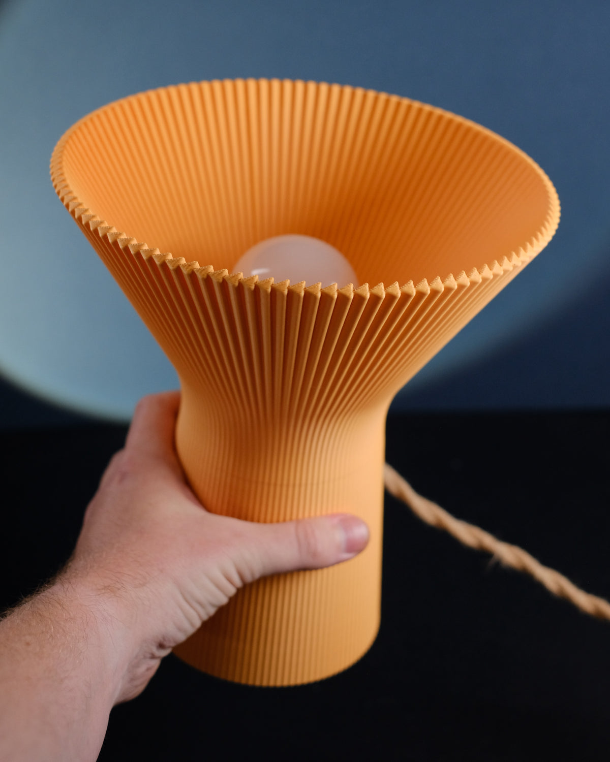 Orange inverted funnel lamp softly glowing against a dark blue background.