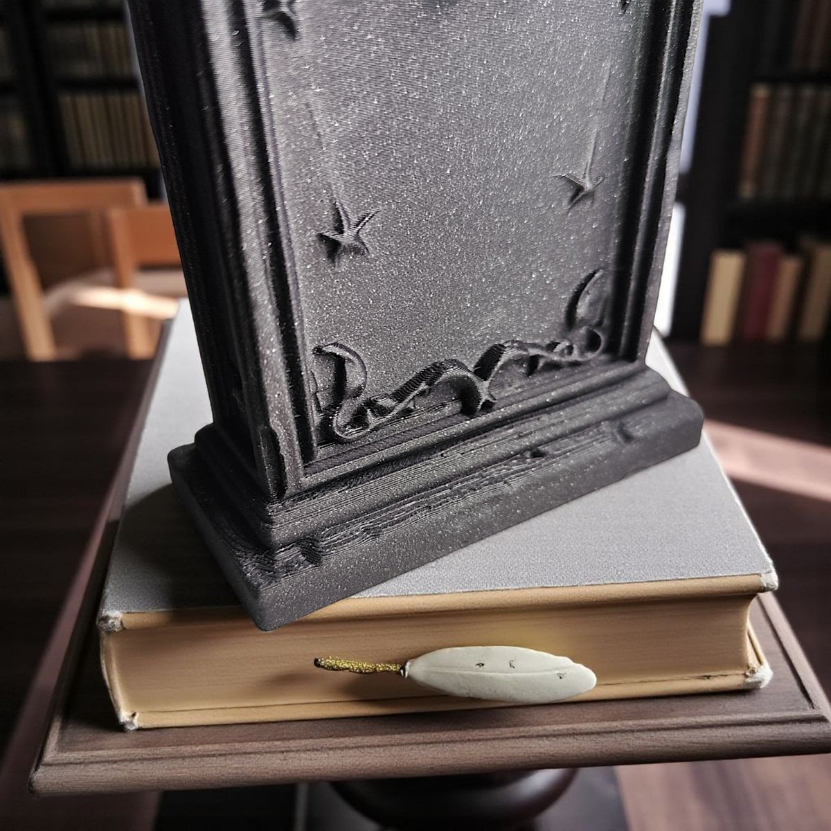 Grey gothic tombstone ornament on dark wooden library desk with books and quill lifestyle