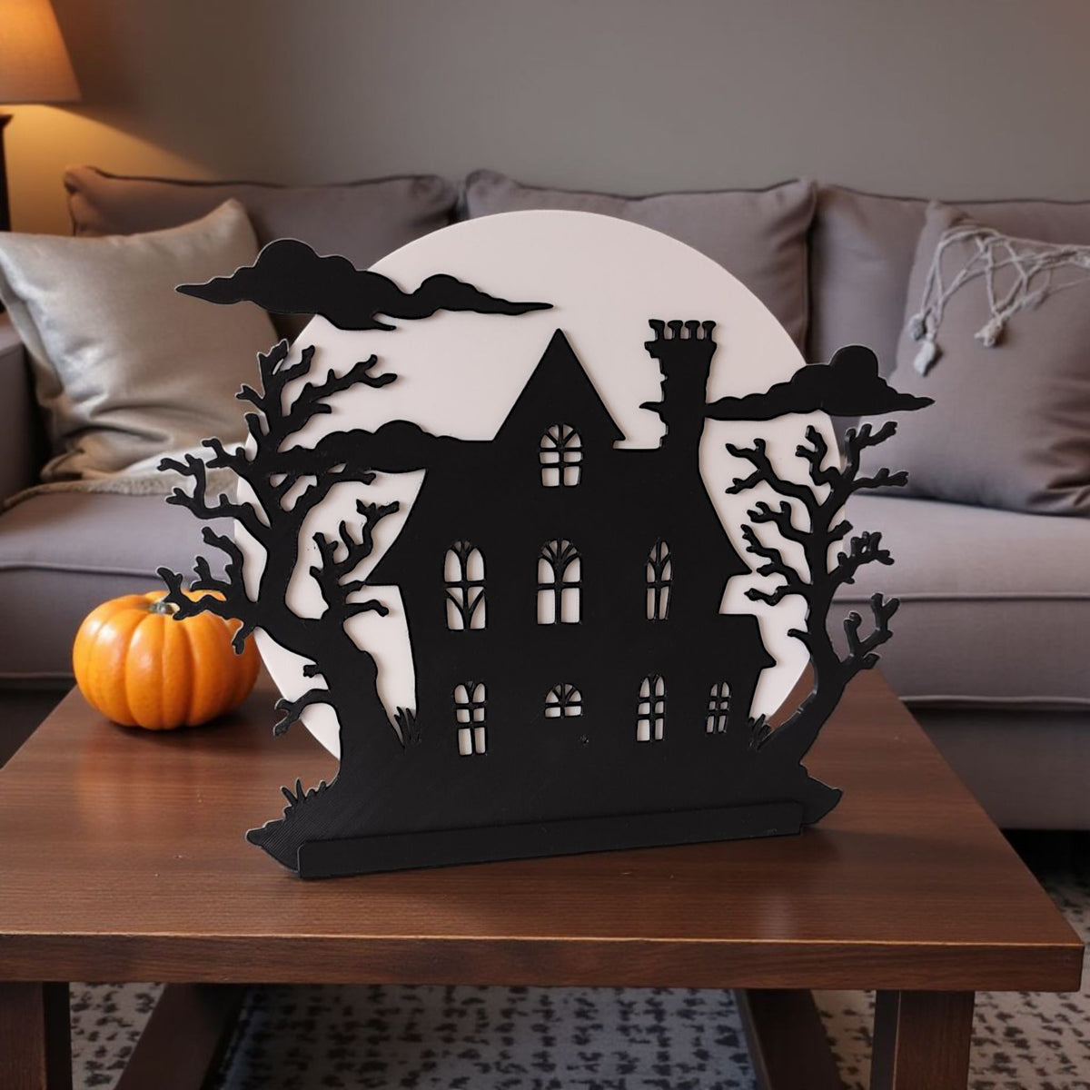 Black 3D printed haunted house decoration on dark dresser with candle and autumn leaves