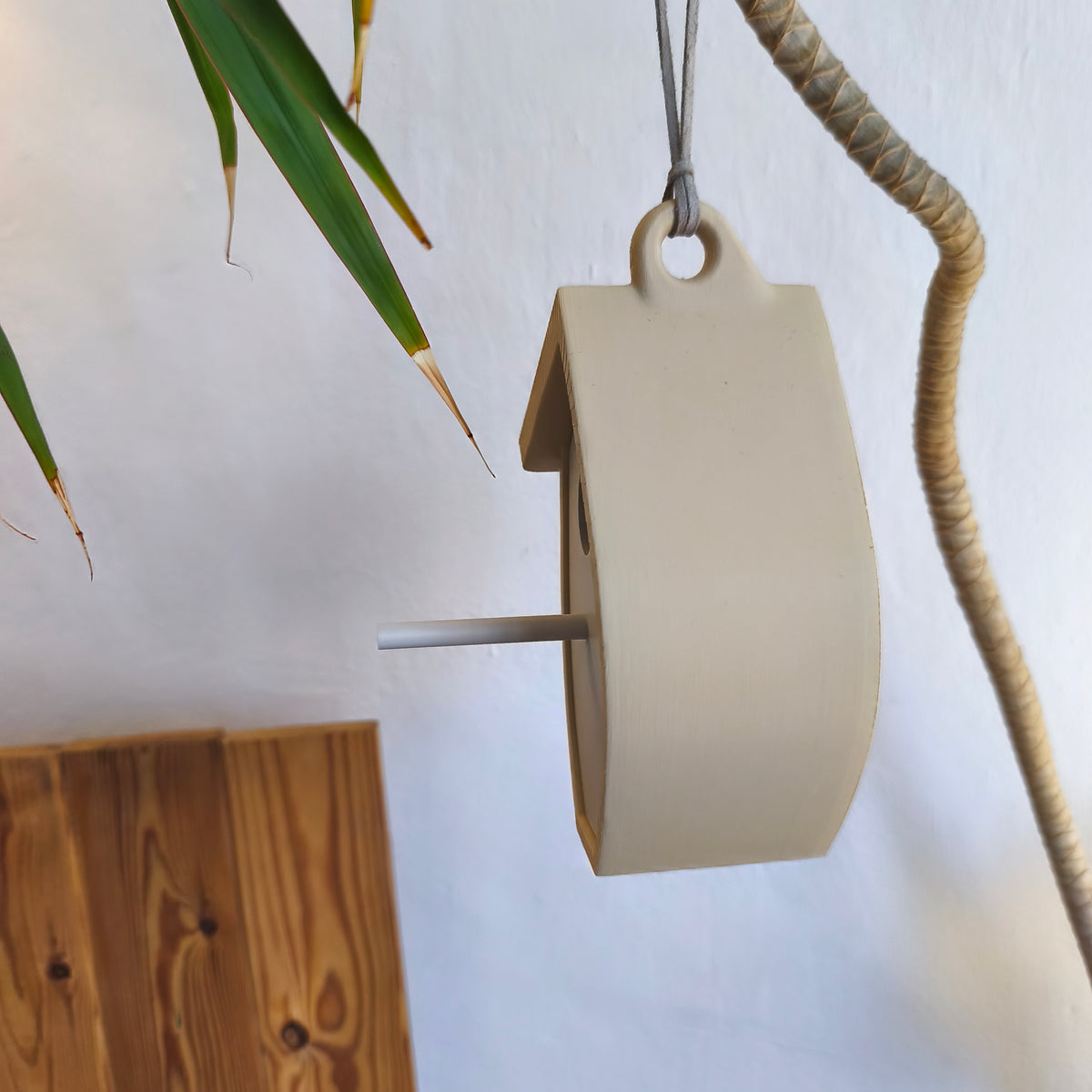 Pale leaf-shaped birdhouse hanging with circular opening and perch