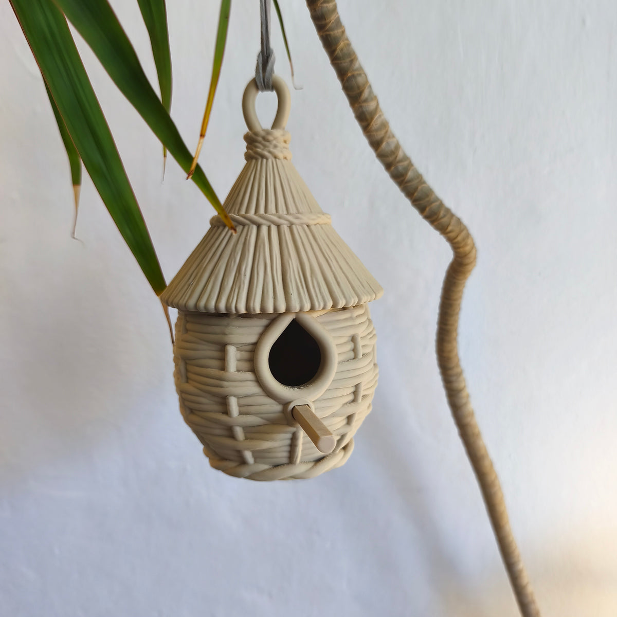 Pale woven-look birdhouse hanging among leaves