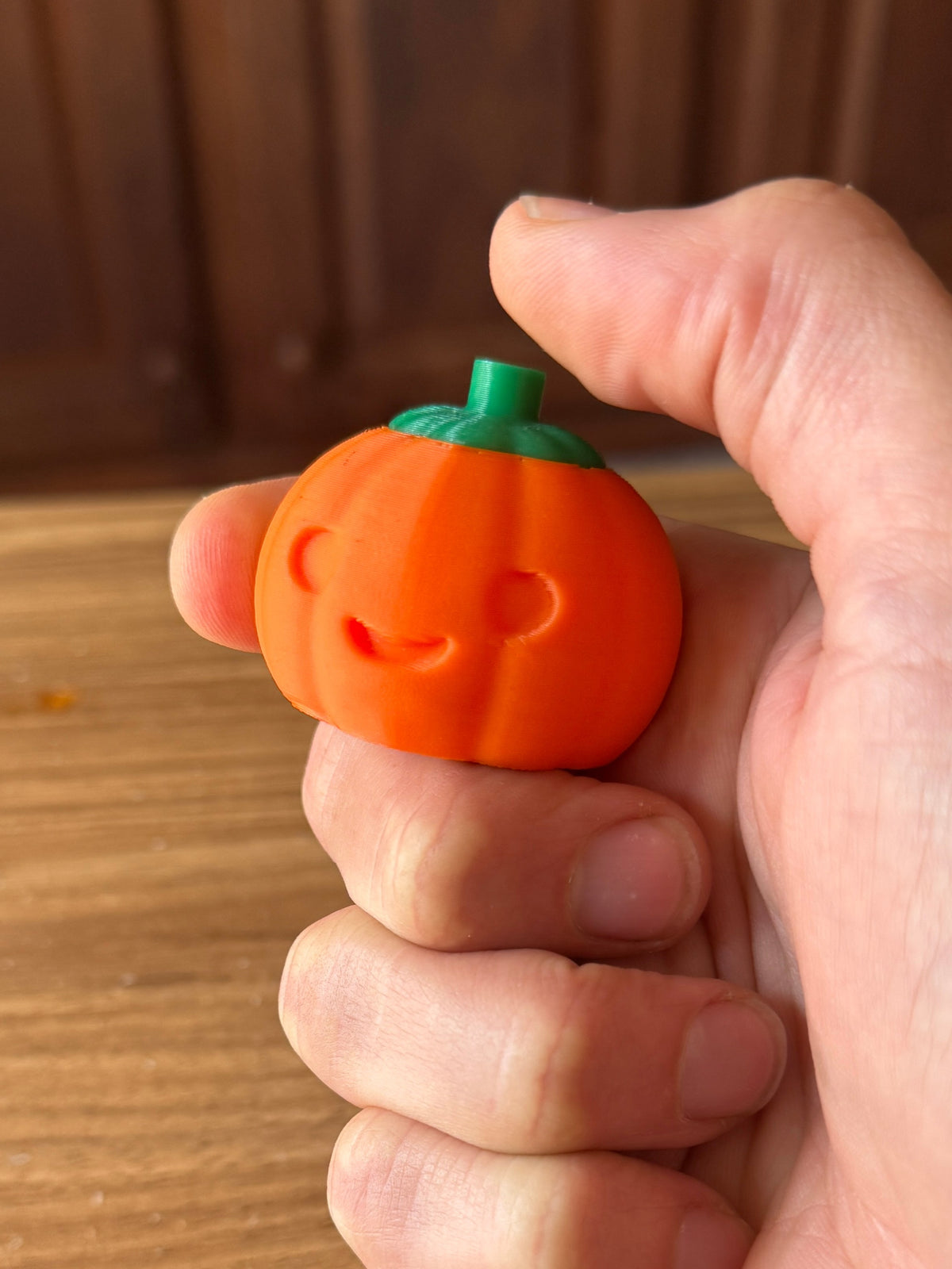 Small orange pumpkin clicker with a green top, held in a hand.