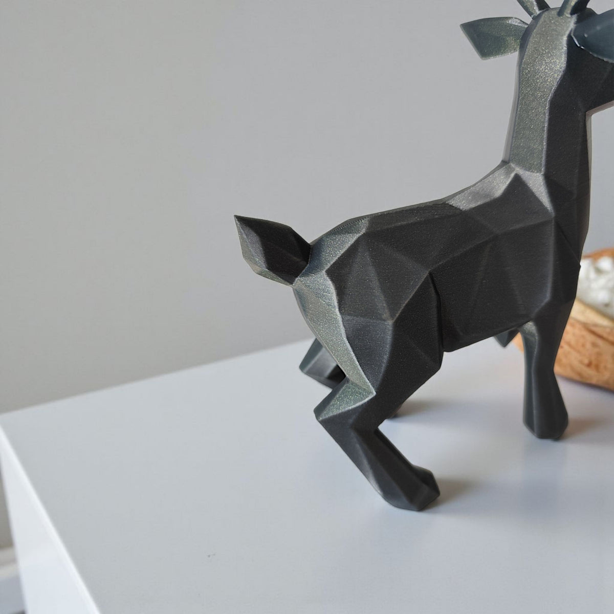 Dark charcoal low poly reindeer on white table with Christmas tree background