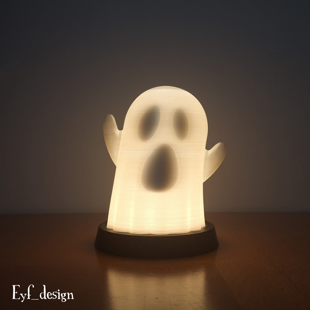 White ghost lamp glowing with its eyes and open mouth revealed on a black base