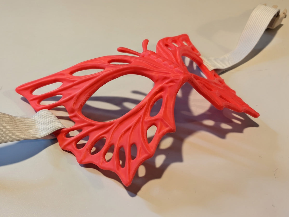 Model wearing the red Butterfly Mask with its broad wings, eye openings and raised vein detail; the strap is not included.
