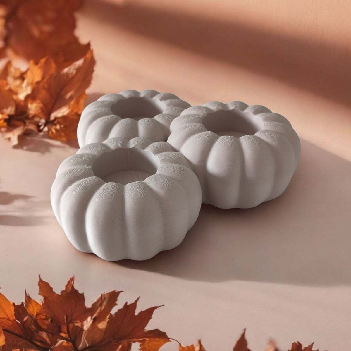 Three white pumpkin tealight holders on white surface with dried autumn branches
