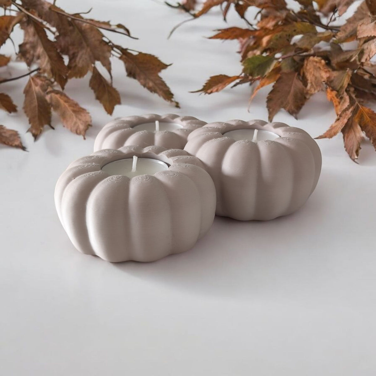 Three white pumpkin tealight holders glowing with lit candles outdoor autumn scene