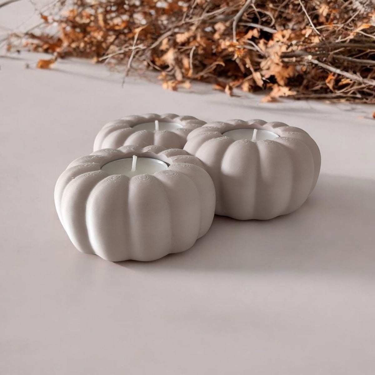 Three white pumpkin tealight holders glowing on dark wood with autumn leaves and pumpkin