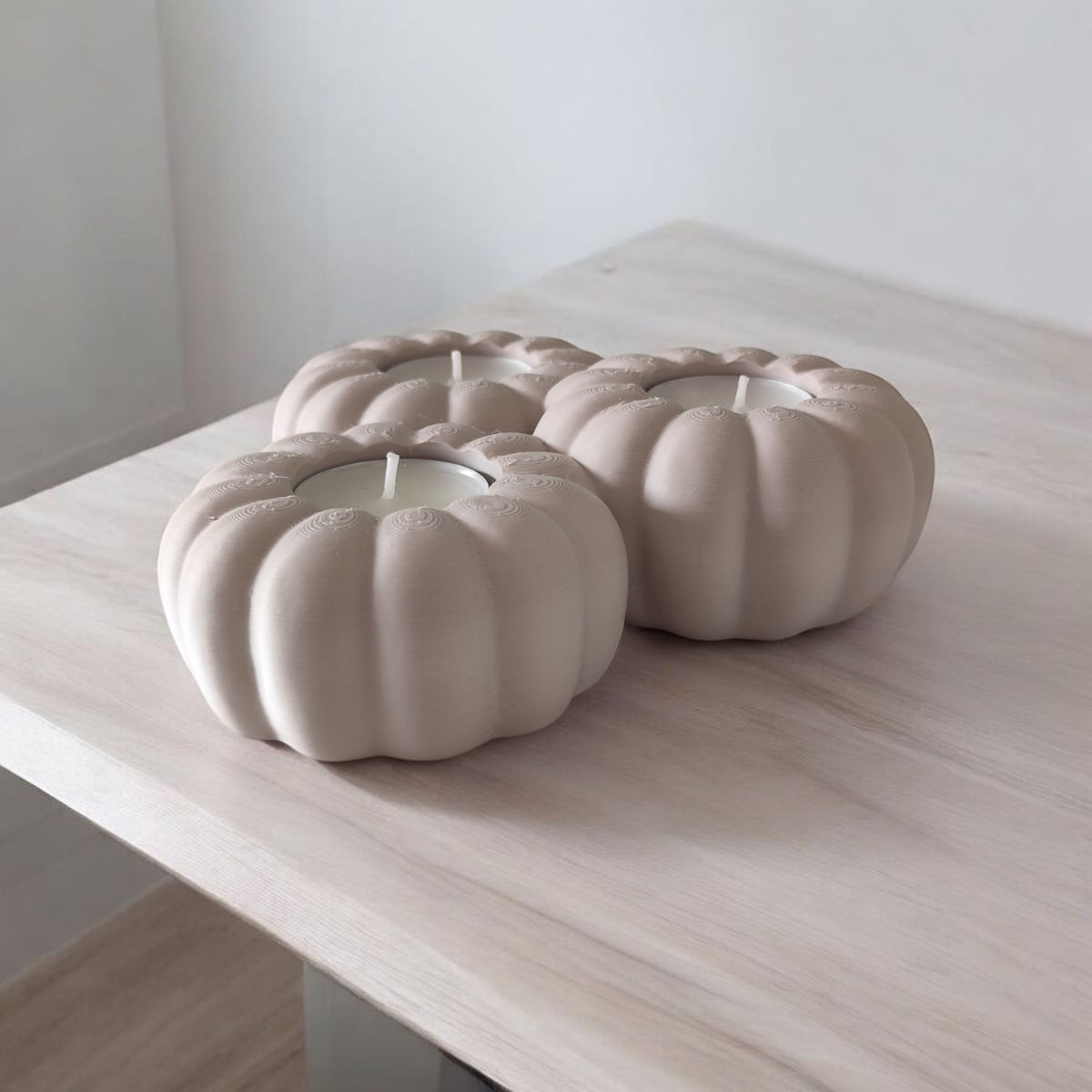 Three white pumpkin tealight holders glowing on wood slice with autumn leaves