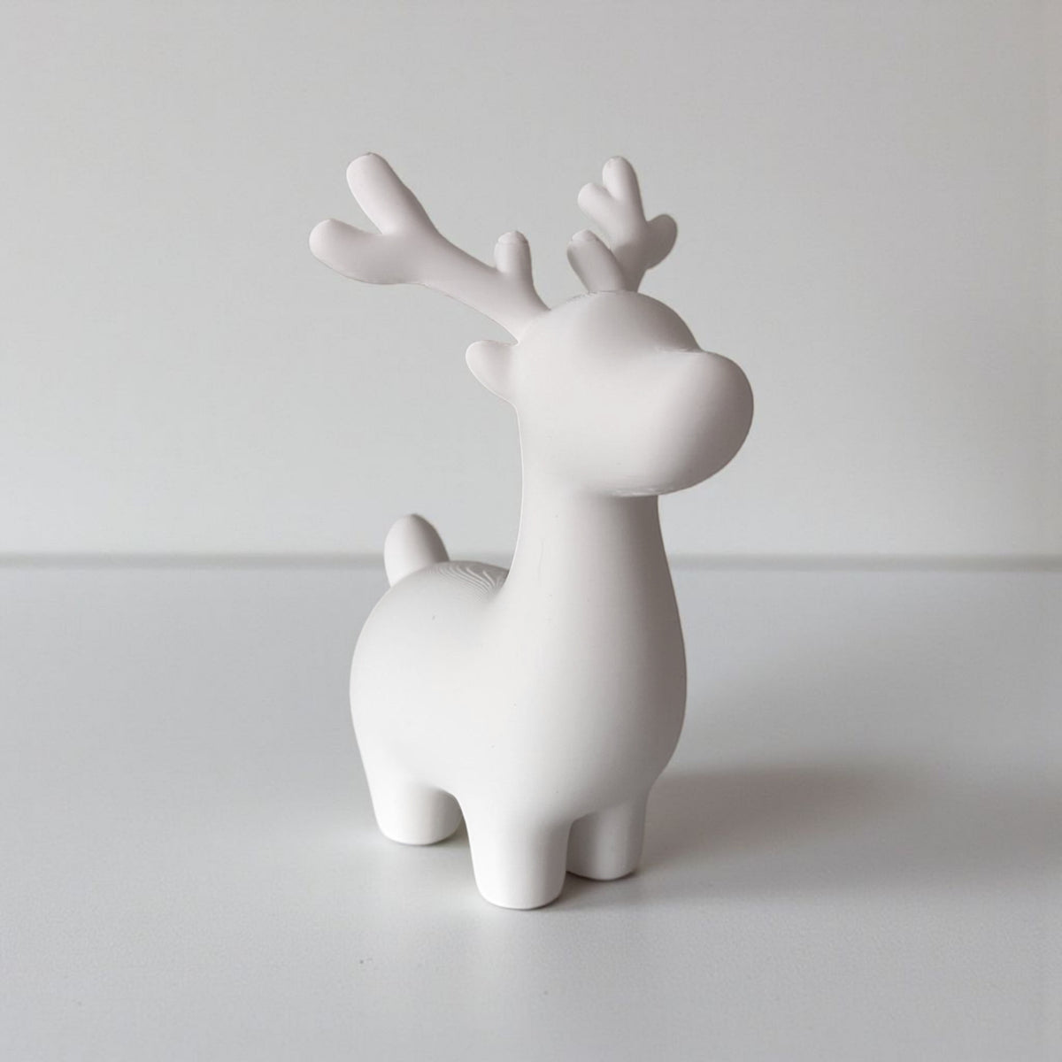 Grey and white reindeer pair on bright windowsill with pine cones and greenery