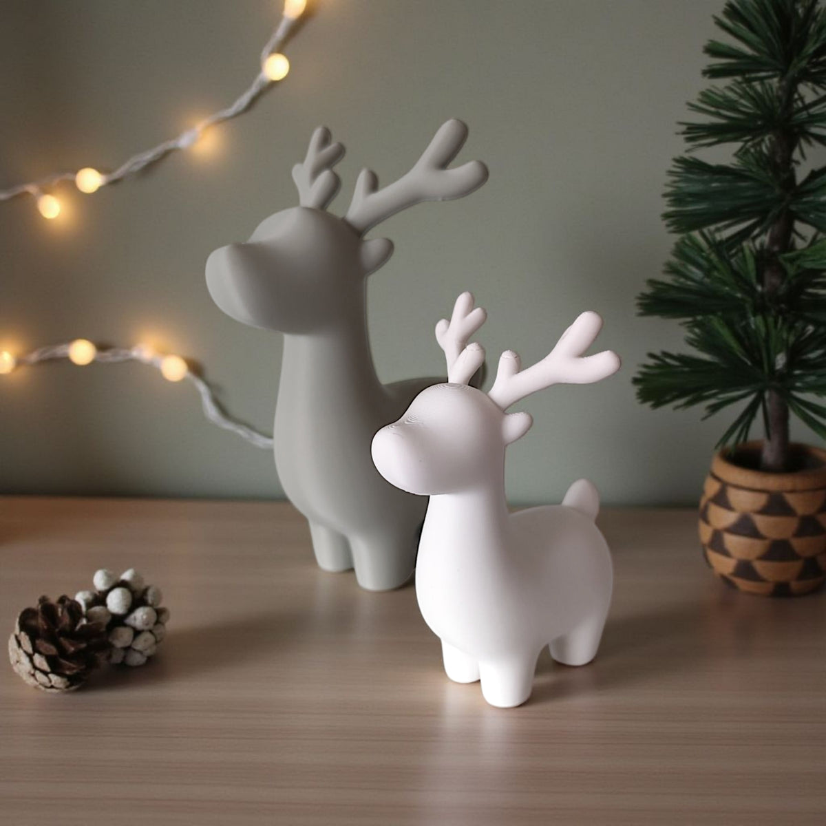 Grey and white reindeer pair on windowsill with gold and red baubles and pine sprigs