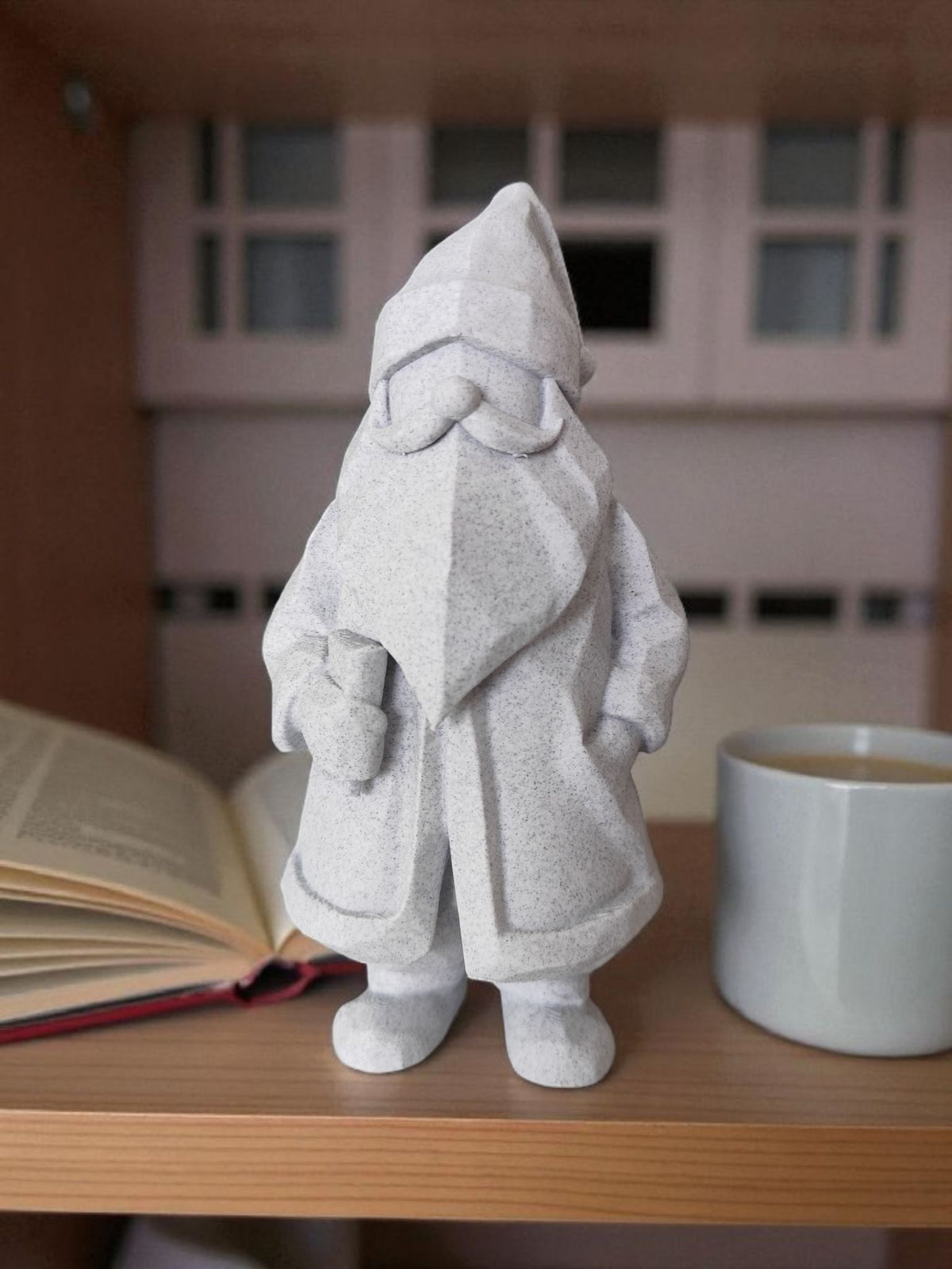 Minimalist low-poly white Santa Claus sculpture on wooden shelf beside mug and open book