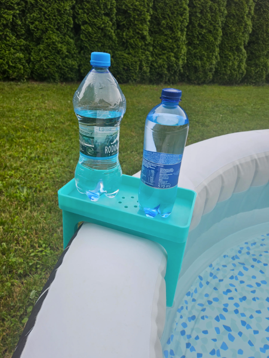 Hot Tub Caddy — teal clip-on side tray holding two water bottles clipped onto the edge of an inflatable hot tub in a garden