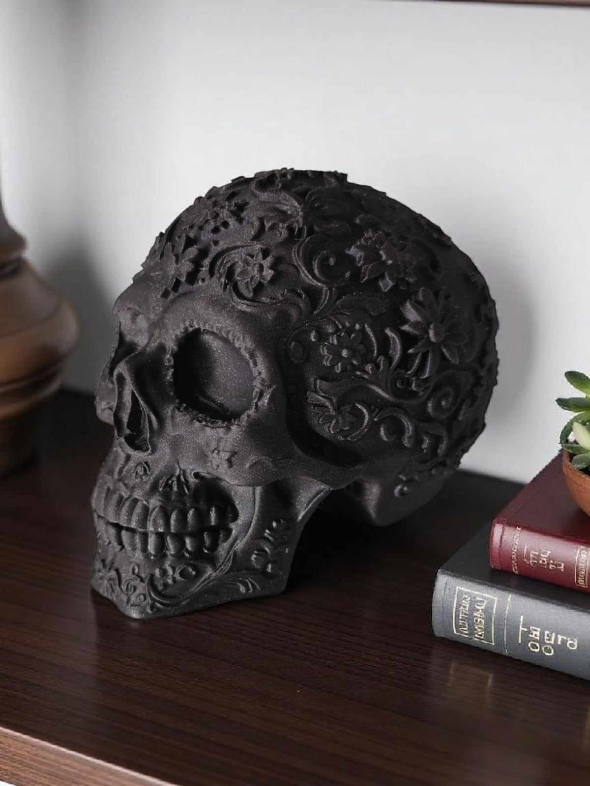 Matte black Mexican skull on dark wooden shelf with vintage books and succulent close up lifestyle