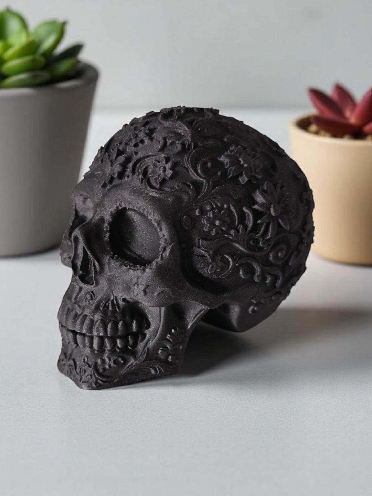 Matte black Mexican ornamental skull with succulents on white surface angled shot
