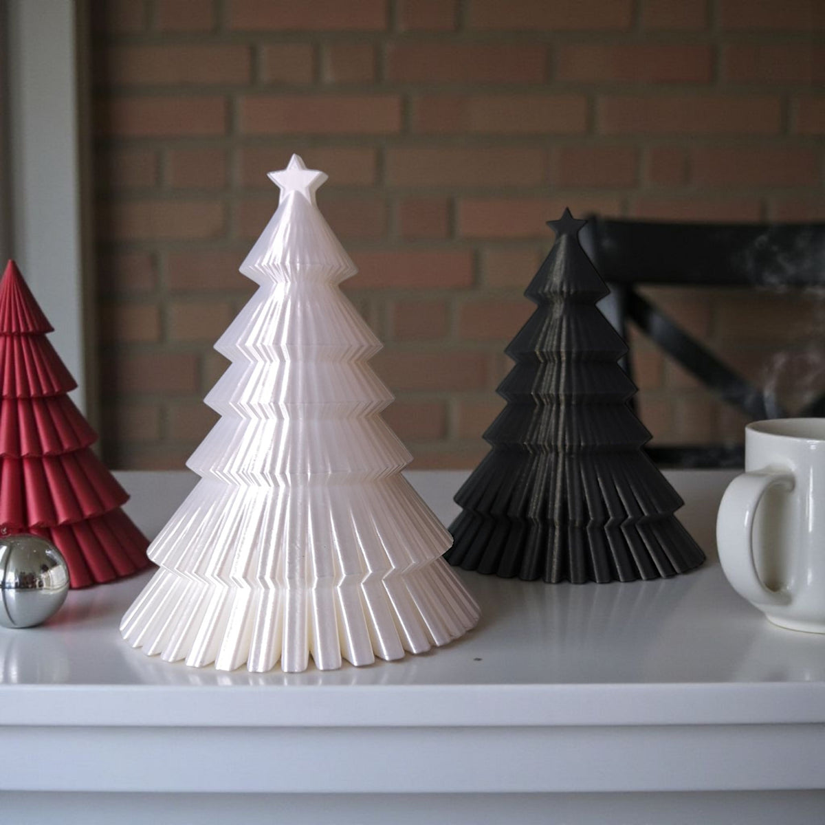 White and black ribbed Christmas tree duo on warm wooden table with coffee and pine cones