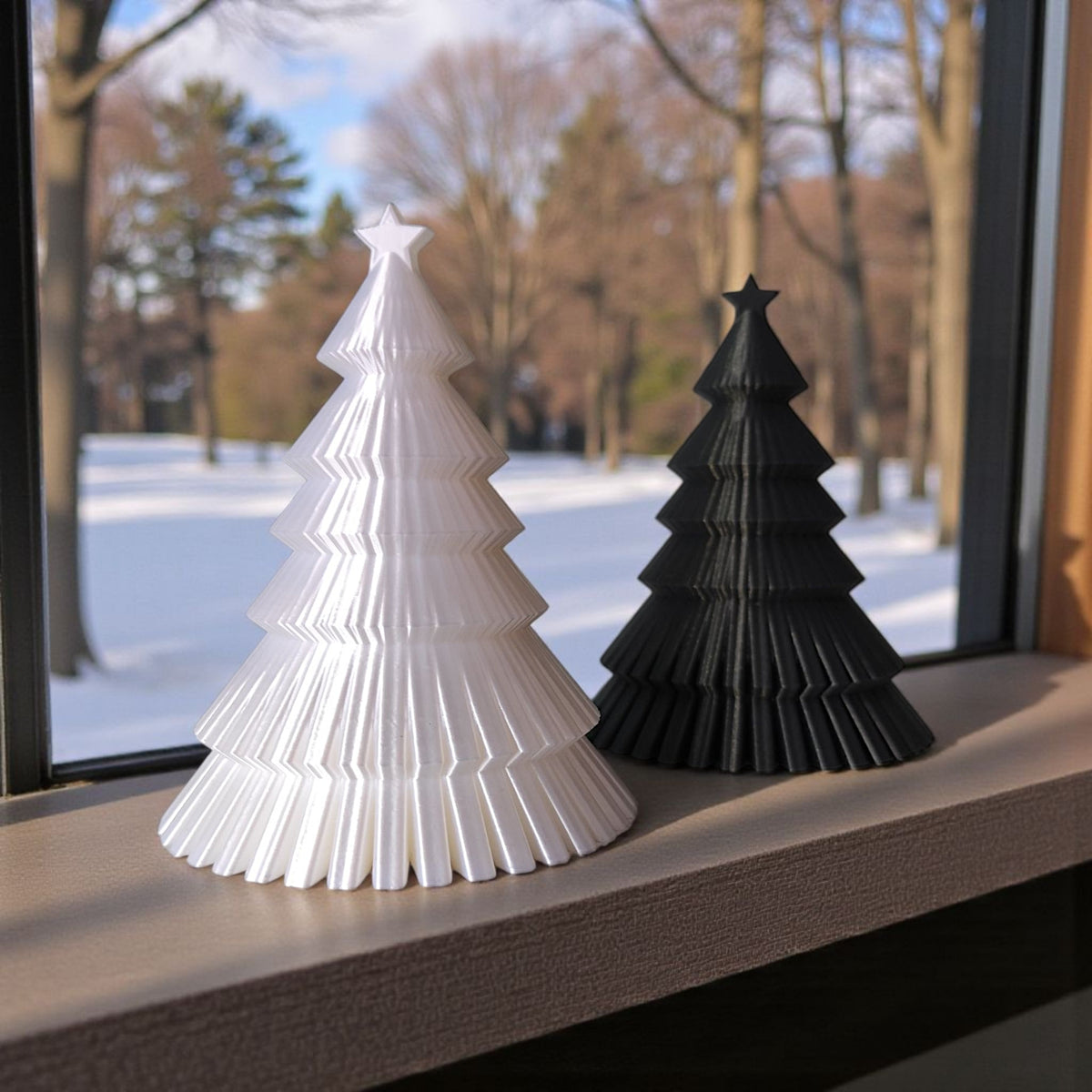 Dark grey ribbed Christmas tree on windowsill beside decorated real Christmas tree