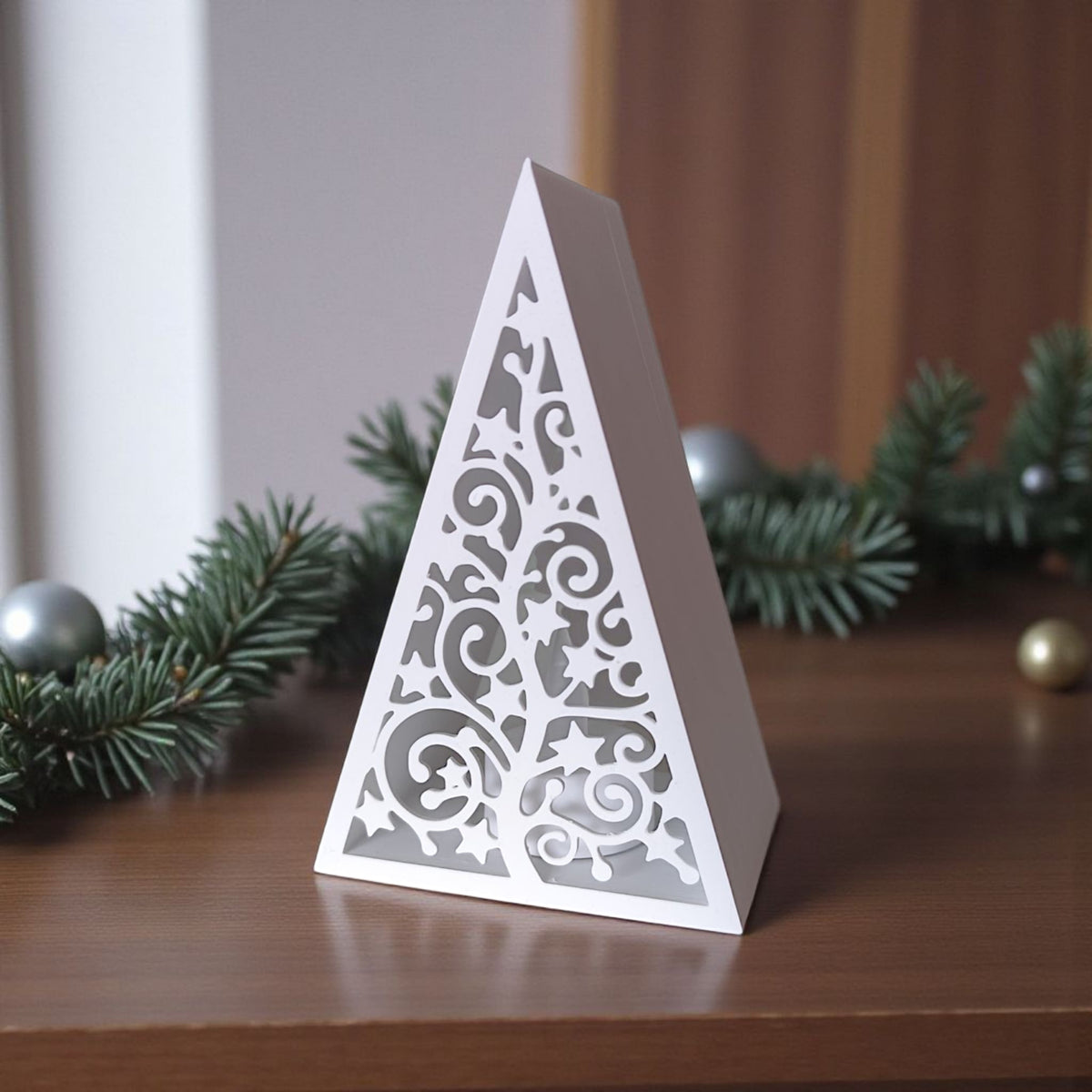 White pyramid Christmas tree lantern with glowing LED tealight and red baubles on wooden table