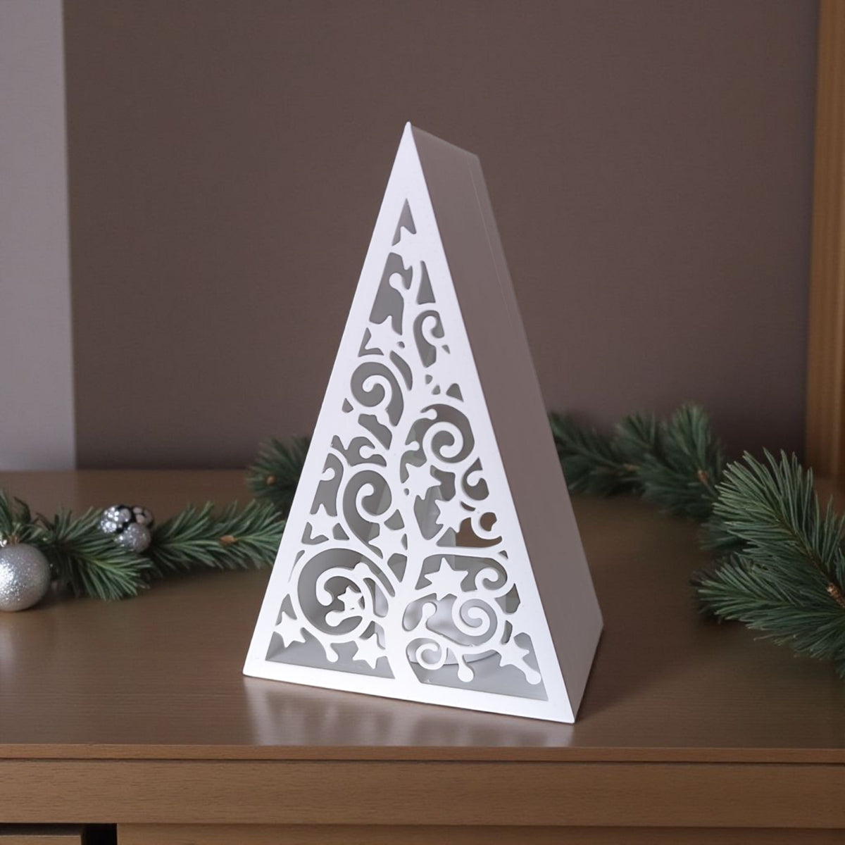 White pyramid lantern with LED tealight beside colourful Christmas baubles