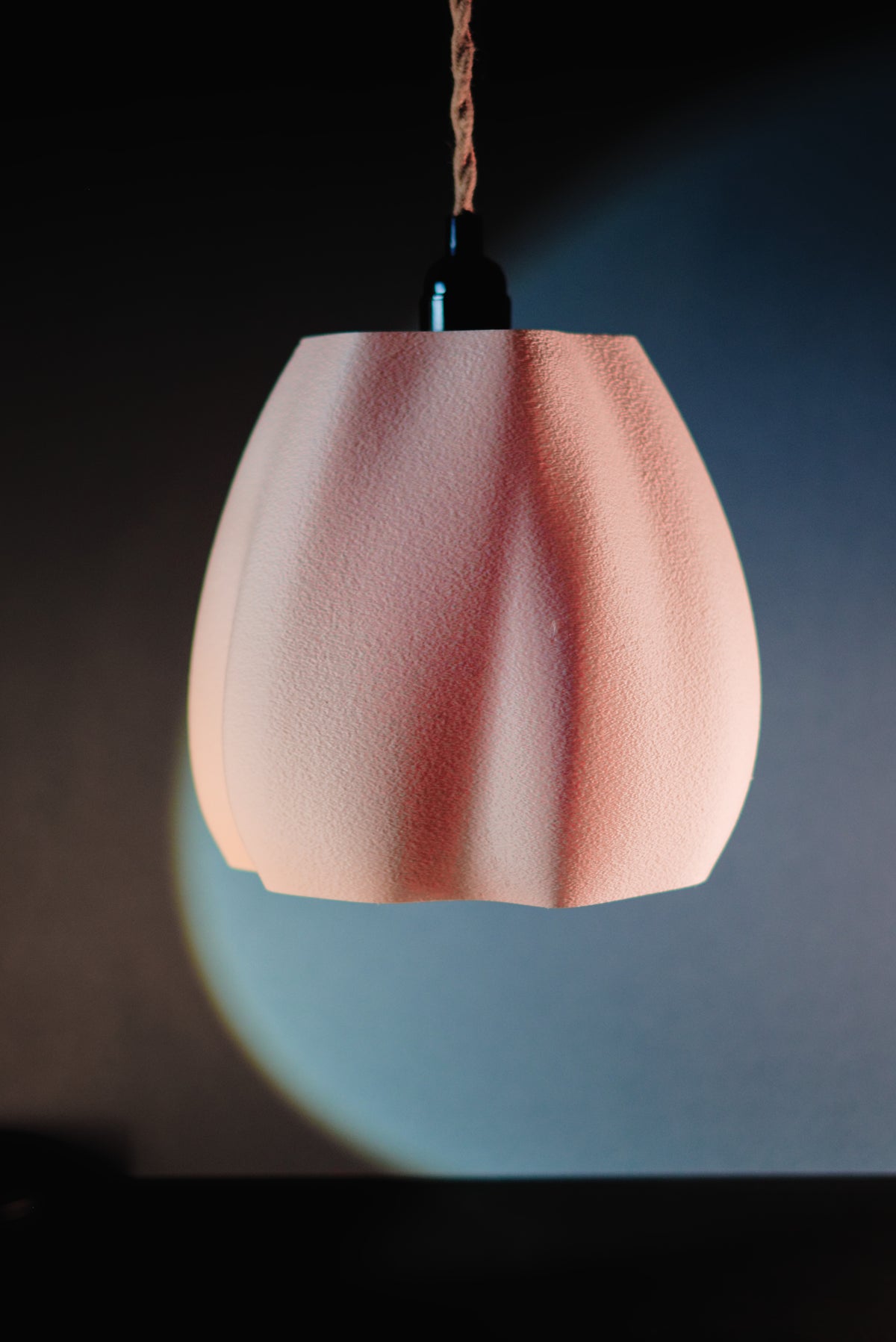 Organic flowing pendant lamp shade pink terracotta hanging with colourful geometric shapes on teal background editorial lifestyle