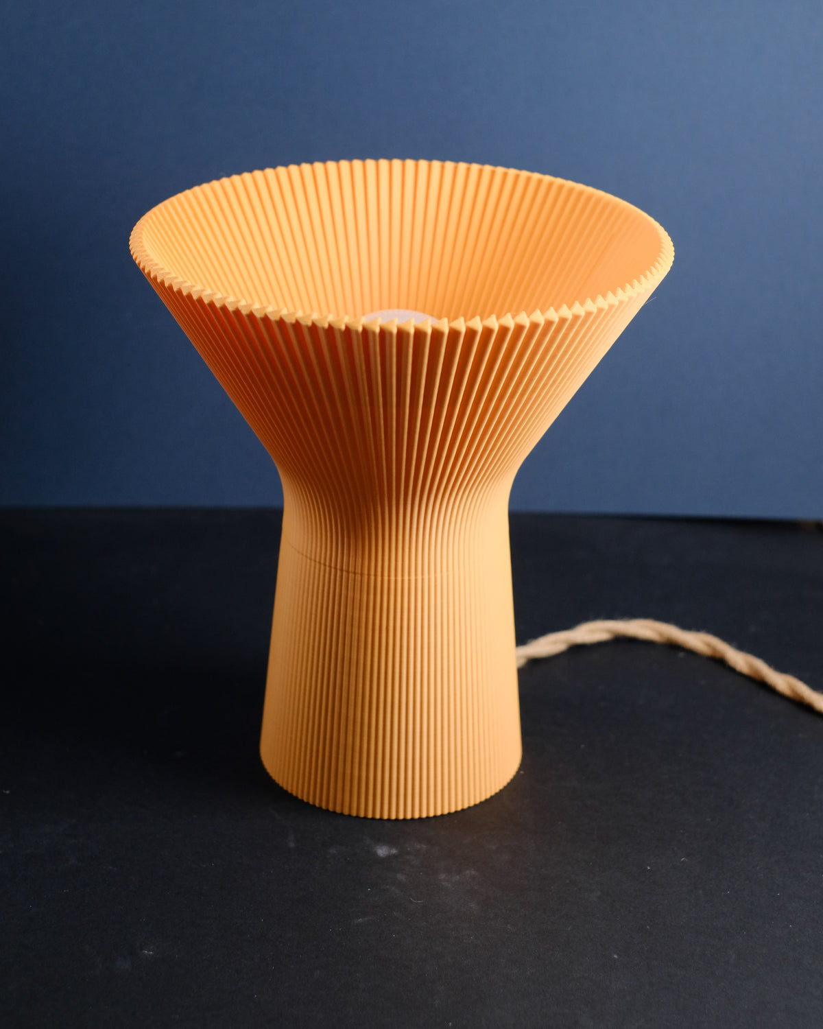 Close-up of the orange pleated inverted funnel lamp glowing from within.