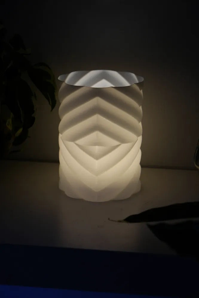 Geometric lampshade glowing warm white at night on a bedside table