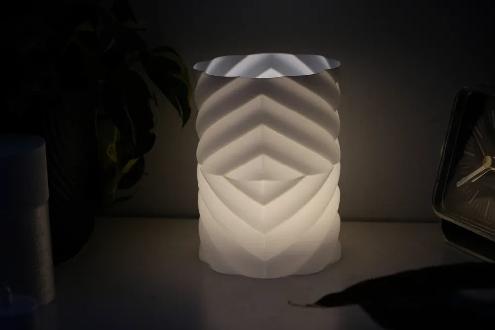 Geometric lampshade glowing warm white next to a clock at night
