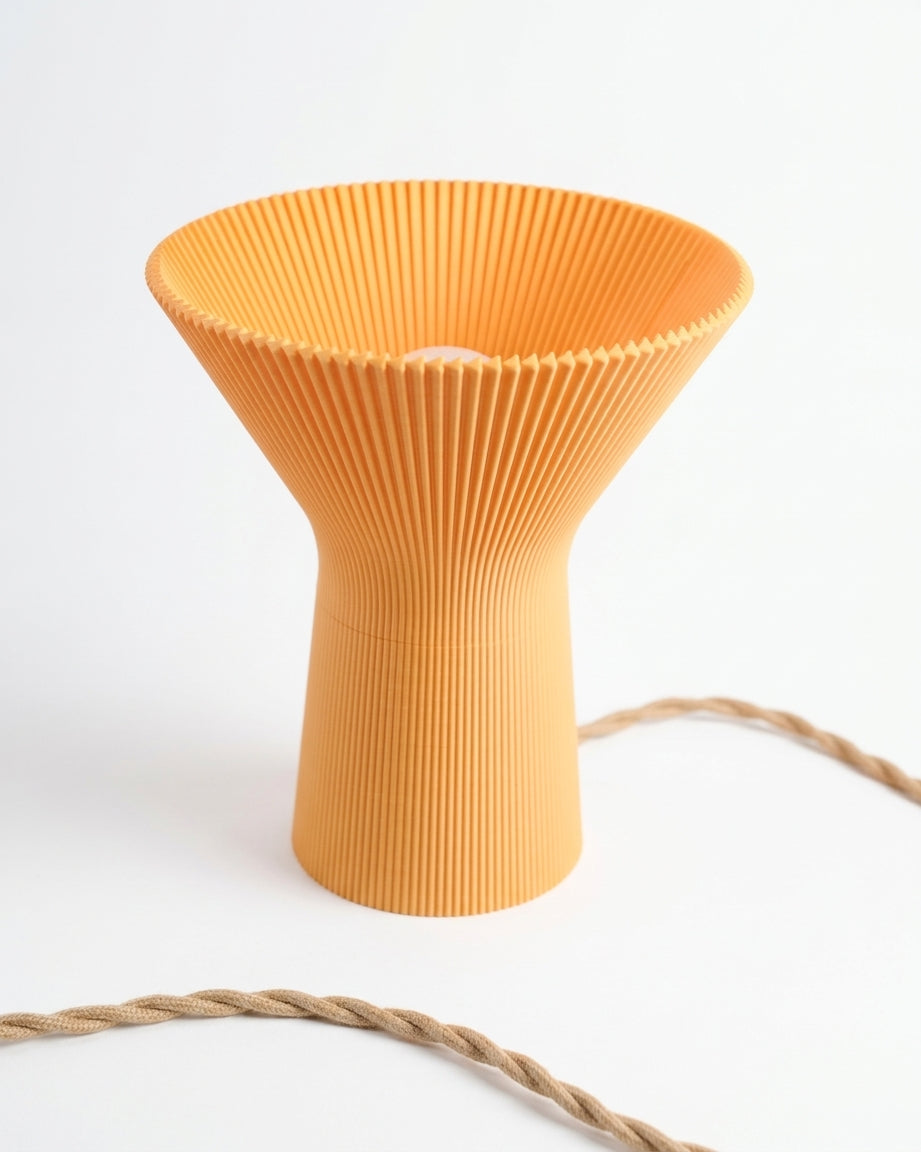 Orange pleated inverted funnel lamp illuminated on a pale surface.