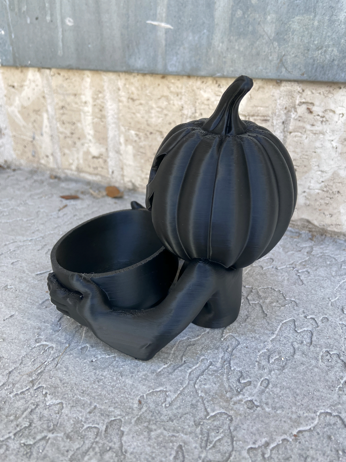 Black pumpkin figure holding a round tray filled with wrapped sweets