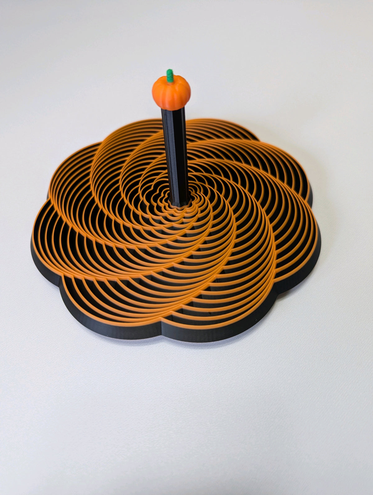 Black flower-shaped Halloween fidget with orange spiral pattern and pumpkin-topped handle