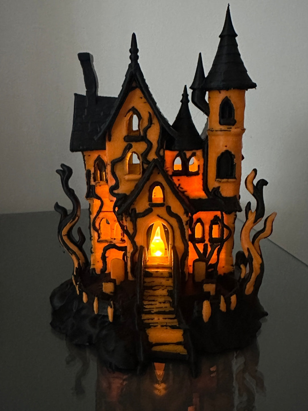 Orange and black haunted house tealight holder with glowing windows, pointed towers, twisted branches and front steps