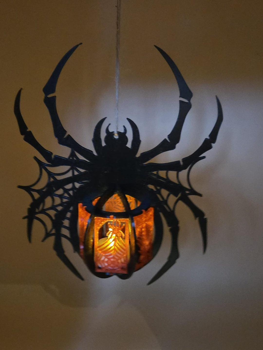 Second view of the black spider-shaped tealight holder with web details and central lantern glow; display string is not included