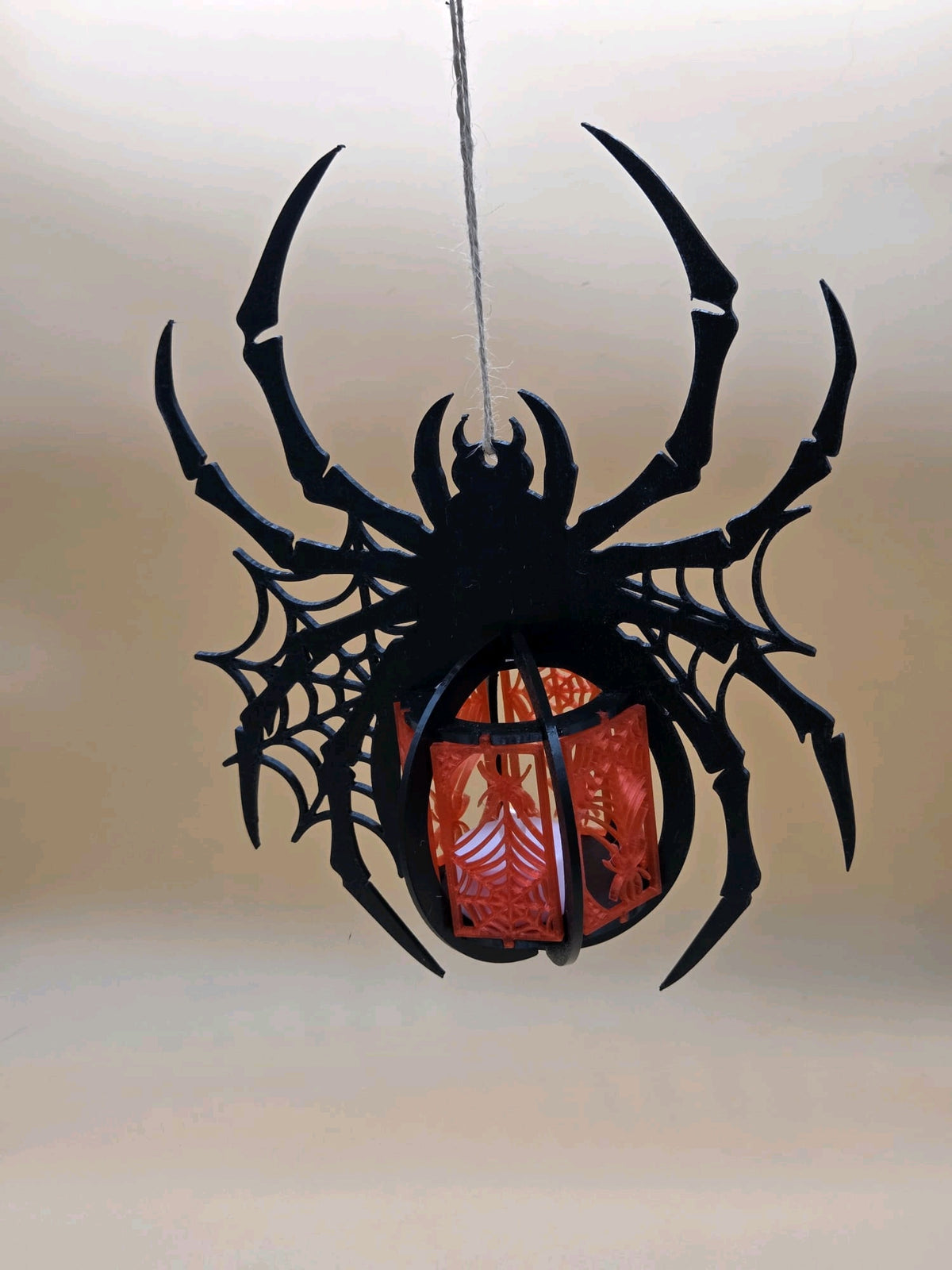 Black hanging spider tealight holder with a glowing central lantern body, suspended from a display string that is not included