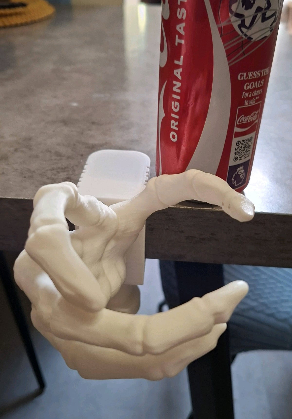 White skeletal hand holder gripping a drinks can at a table edge