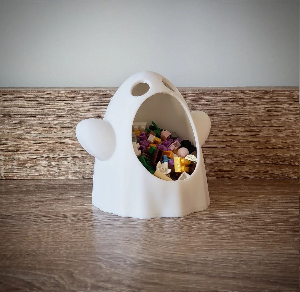 White wide-mouthed ghost sweet bowl filled with small colourful pieces on a wood tabletop, angled view