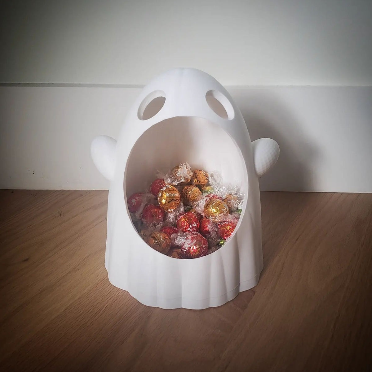 White wide-mouthed ghost sweet bowl filled with wrapped chocolates, close-up on a darker wood surface