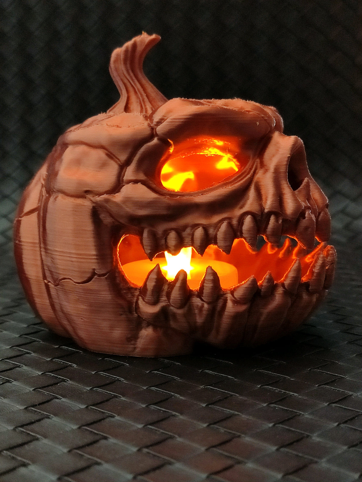 Close-up of the brown pumpkin skull tealight holder with warm light glowing through the eyes and mouth