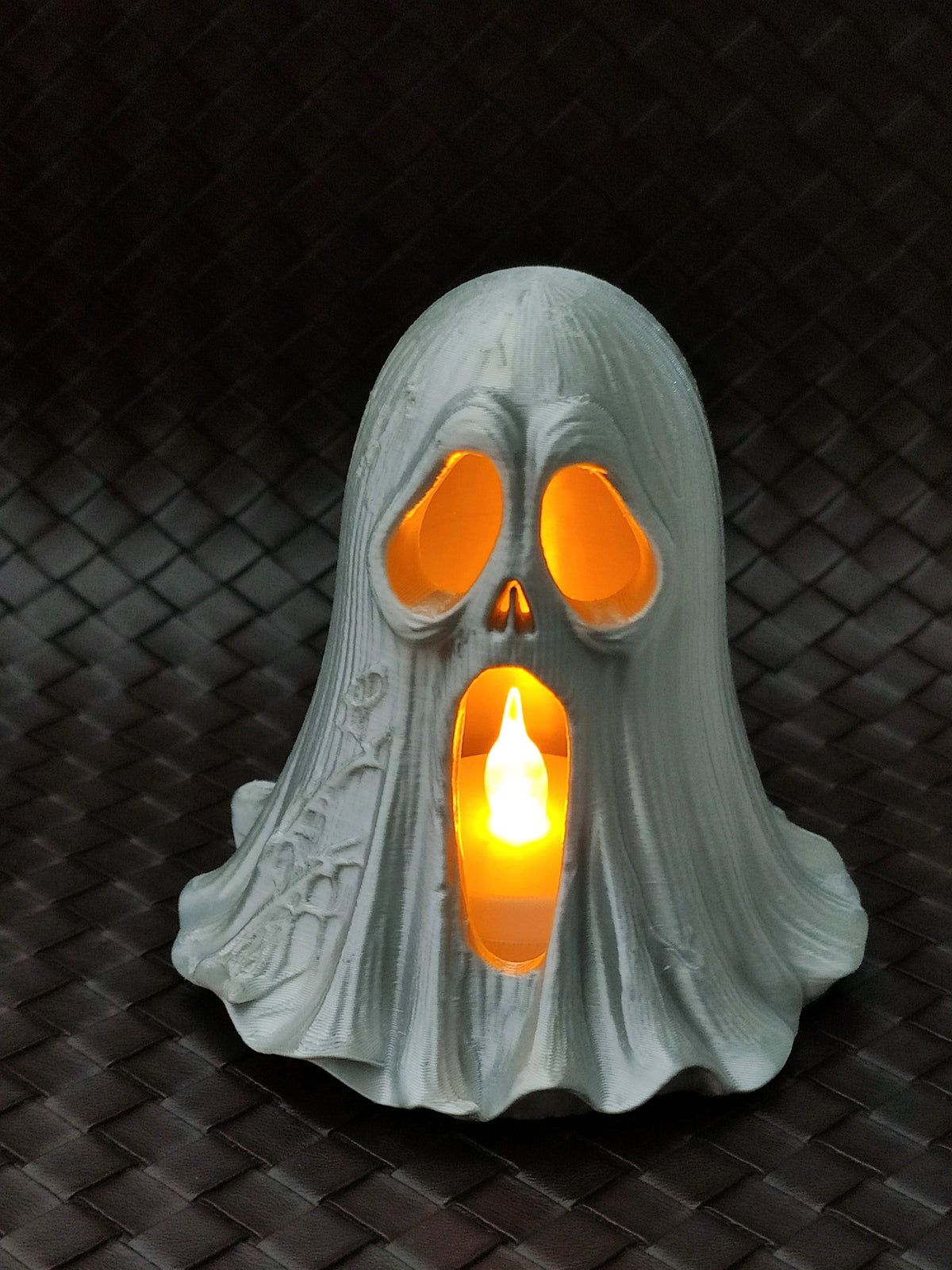 Pale ghost-shaped holder with a skull-like face and orange light glowing through its openings