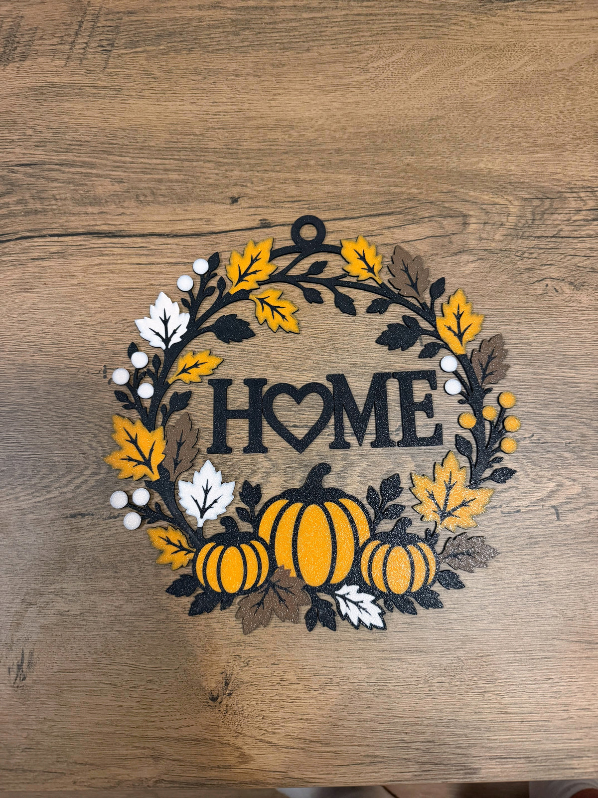 Halloween wreath with pumpkins, autumn leaves and HOME lettering shown flat on a wood surface