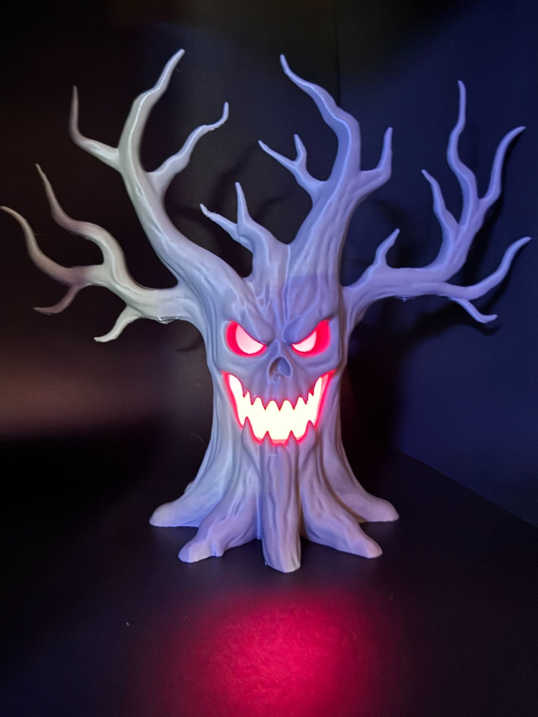 Laughing tree tealight holder with red-lit eyes and grin against a dark background