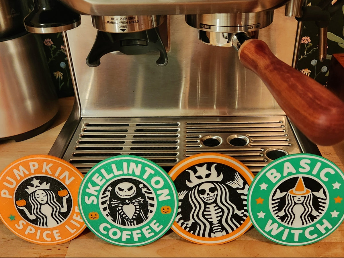Four Halloween coffee coaster designs displayed by an espresso machine