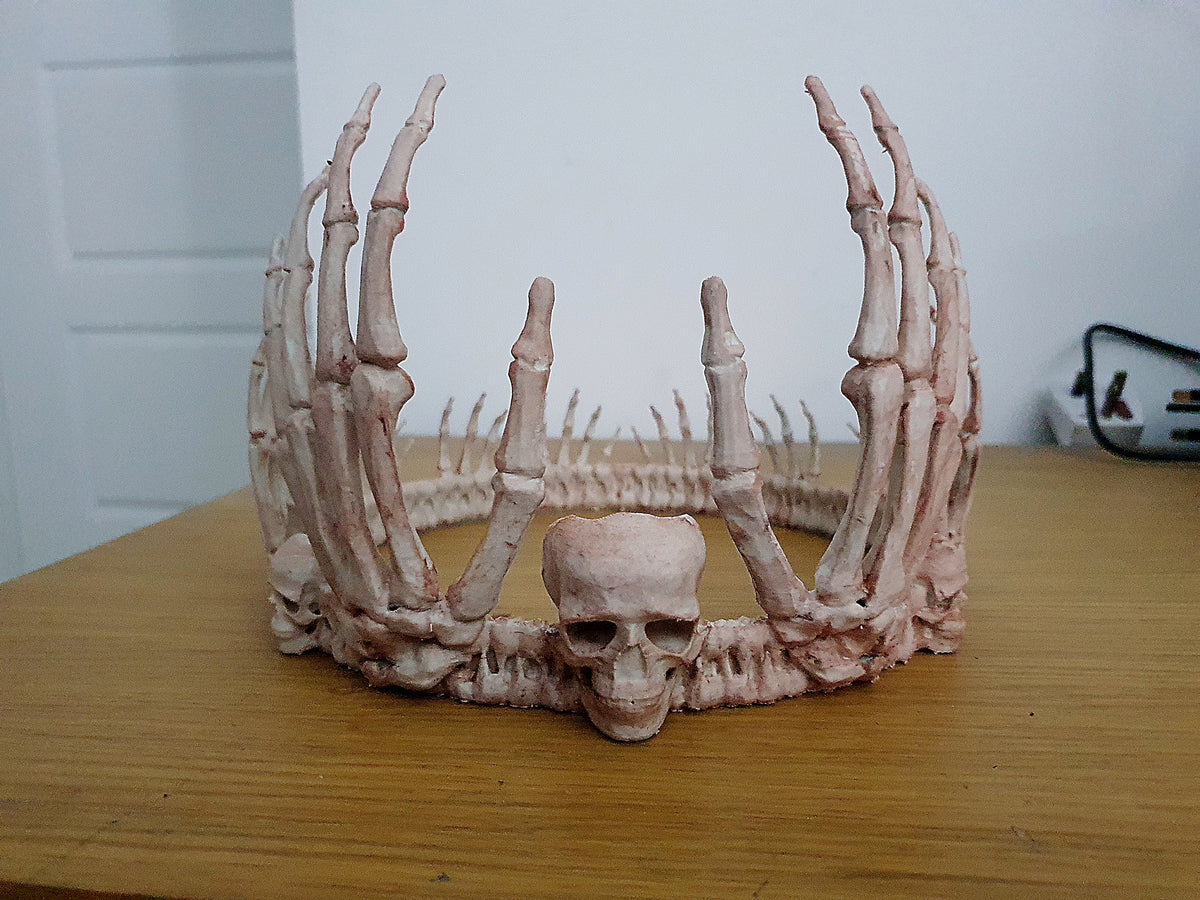 Pale skeleton crown with skeletal fingers rising around a small skull at the front
