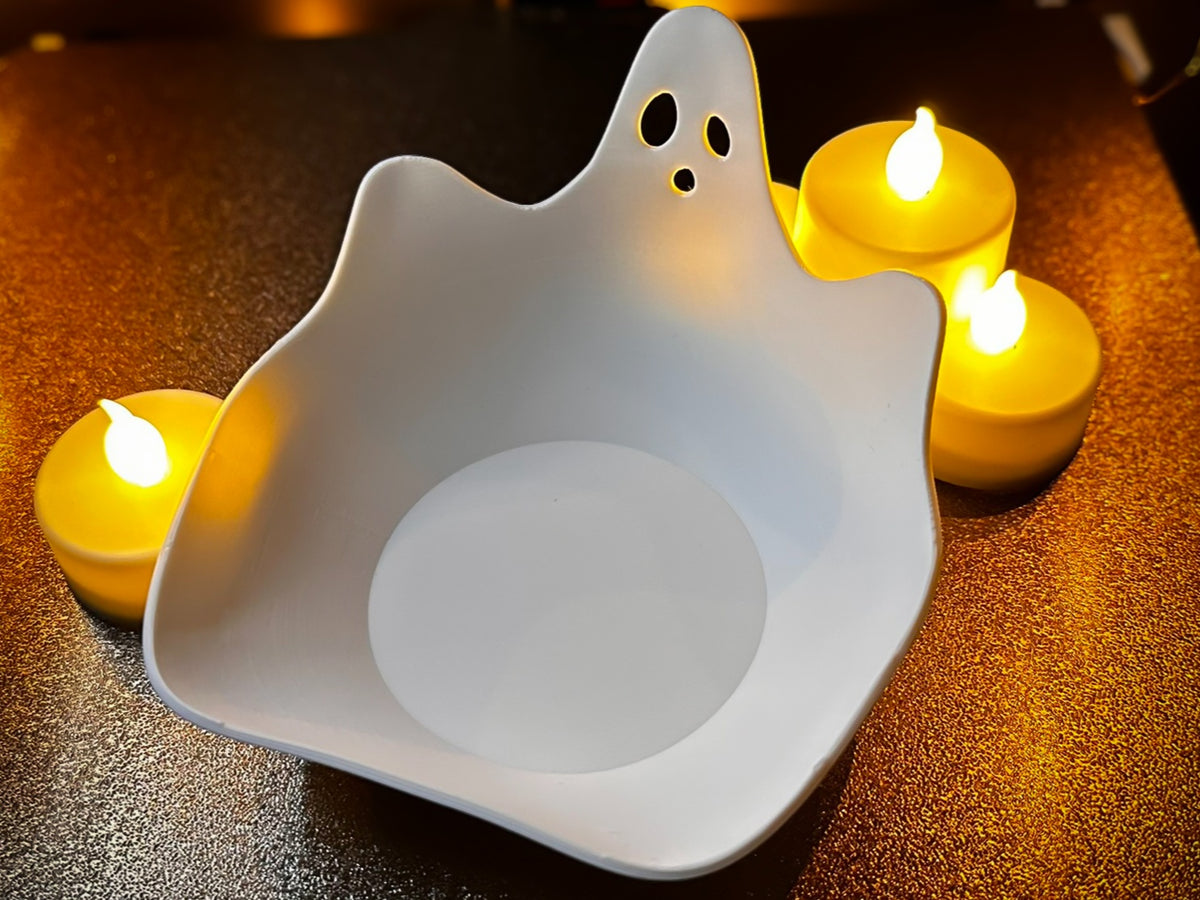 Three white ghost-shaped sweet trays on a dark autumn leaf-patterned cloth