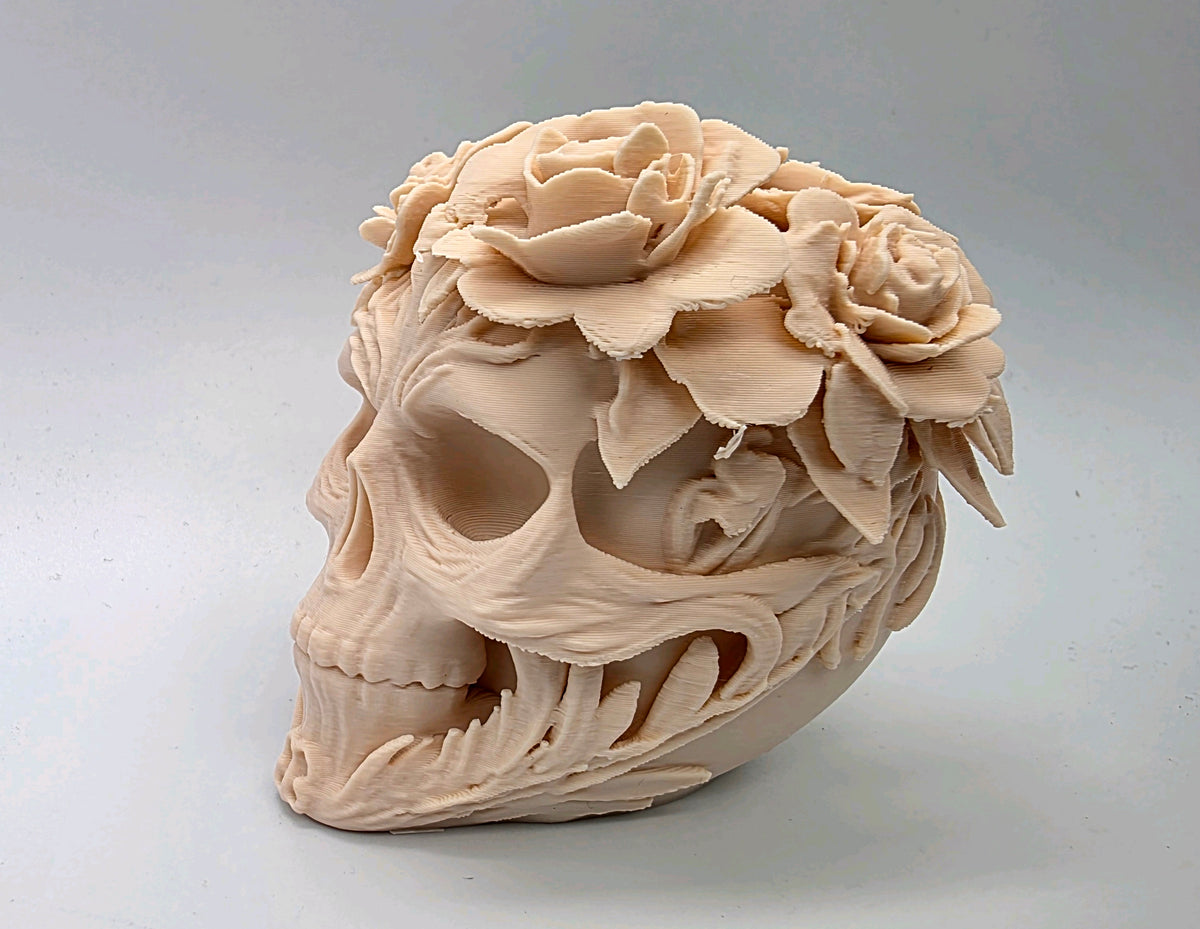 Pale skull sculpture with roses, foliage and a vine-like design around the side