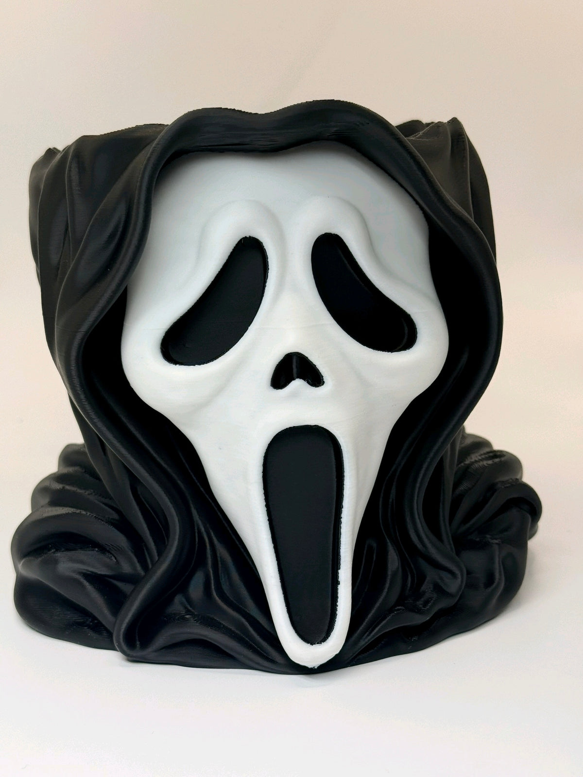 Front view of a black hooded head-shaped sweet bowl with a white screaming mask
