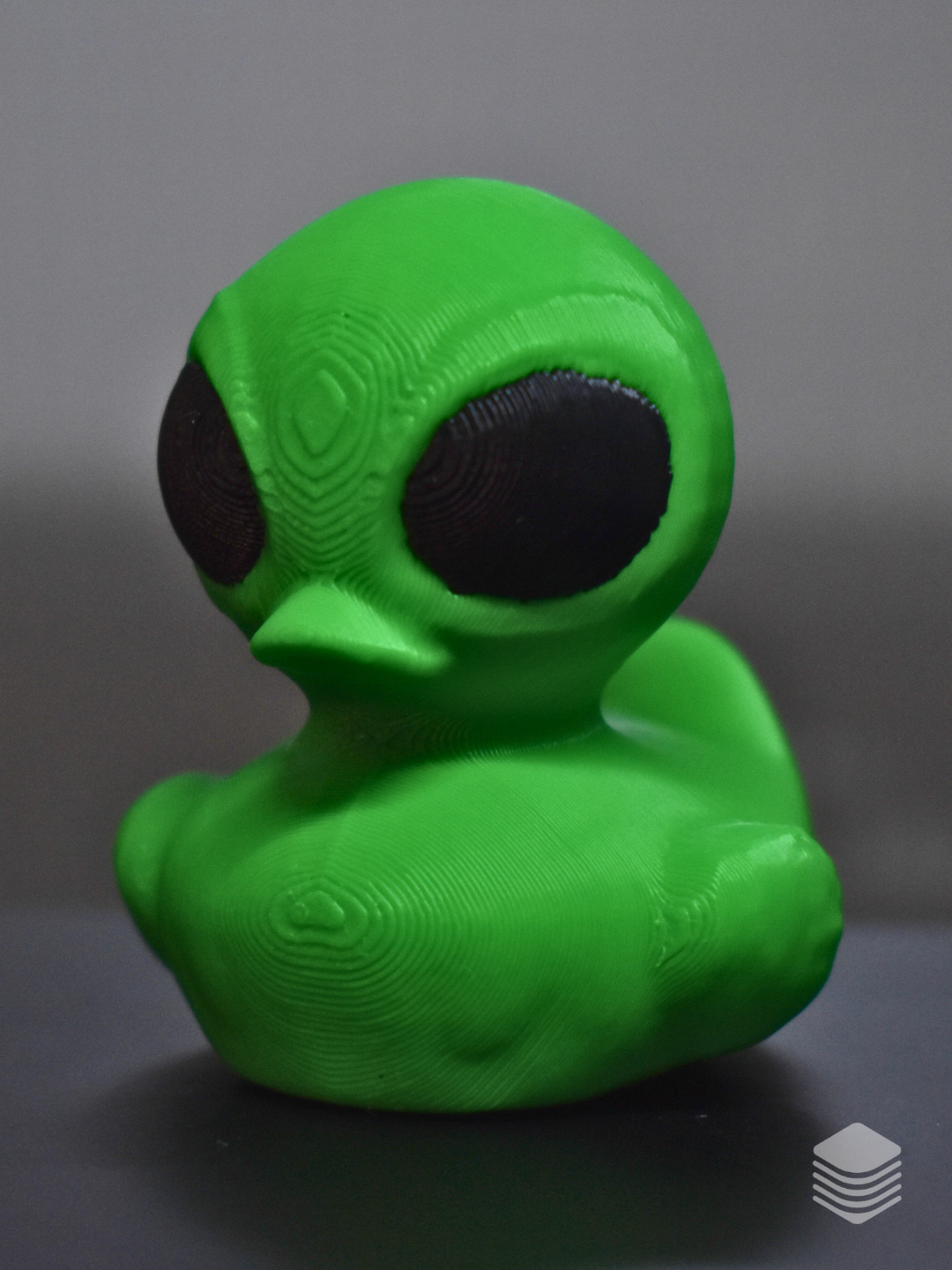 Bright green alien bath duck with oversized black eyes viewed from the side
